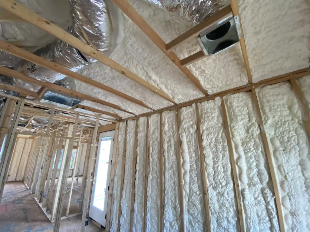 White spray foam insulation is installed between studs after framing.